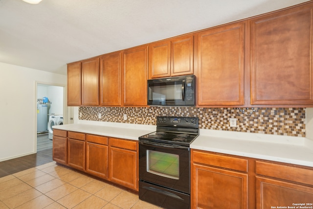 kitchen with water heater, black appliances, washing machine and clothes dryer, light tile patterned flooring, and backsplash