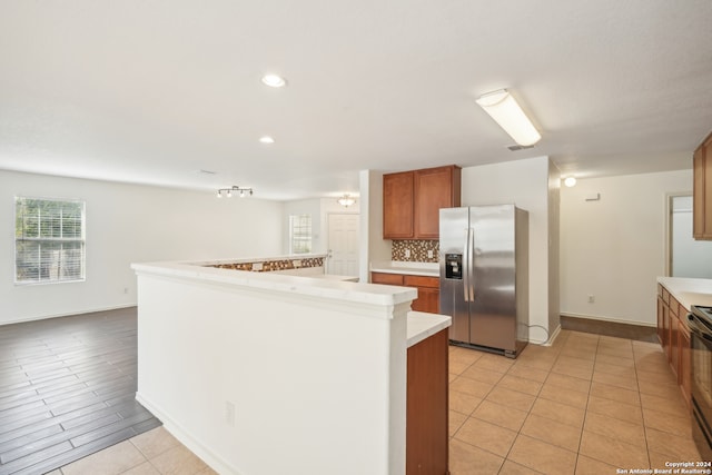 kitchen featuring black electric range, decorative backsplash, light tile patterned floors, stainless steel fridge with ice dispenser, and a kitchen island