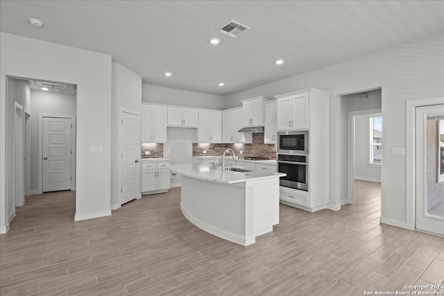 kitchen featuring sink, light wood-type flooring, an island with sink, stainless steel appliances, and white cabinets