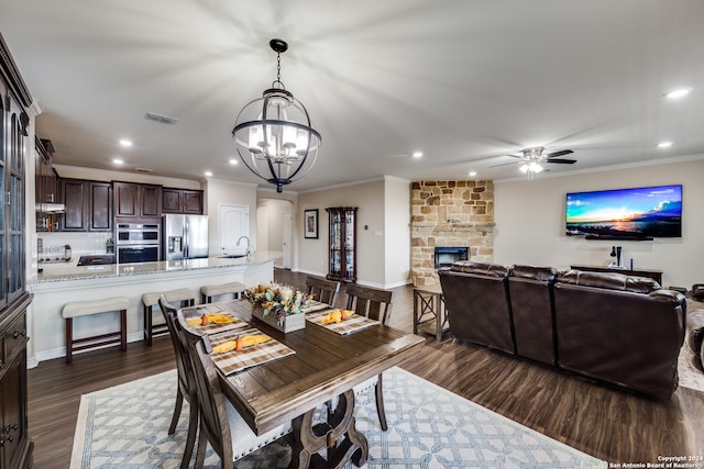 dining room featuring ceiling fan with notable chandelier, a fireplace, crown molding, and dark wood-type flooring