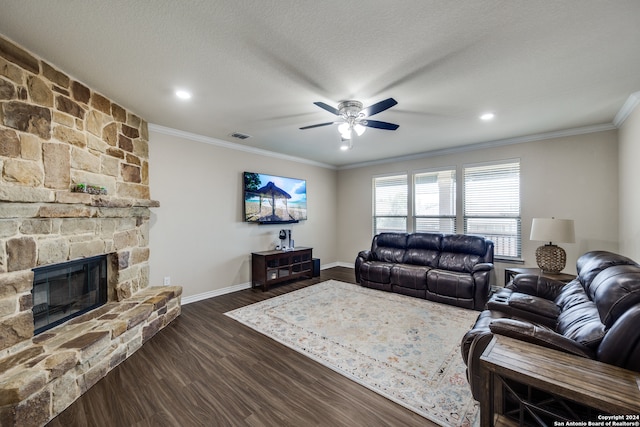 living room with ceiling fan, a stone fireplace, dark hardwood / wood-style flooring, ornamental molding, and a textured ceiling