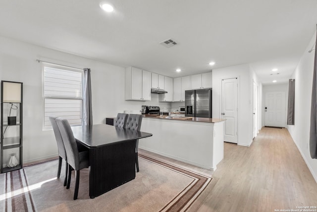 kitchen featuring white cabinets, light hardwood / wood-style flooring, appliances with stainless steel finishes, a kitchen bar, and a healthy amount of sunlight