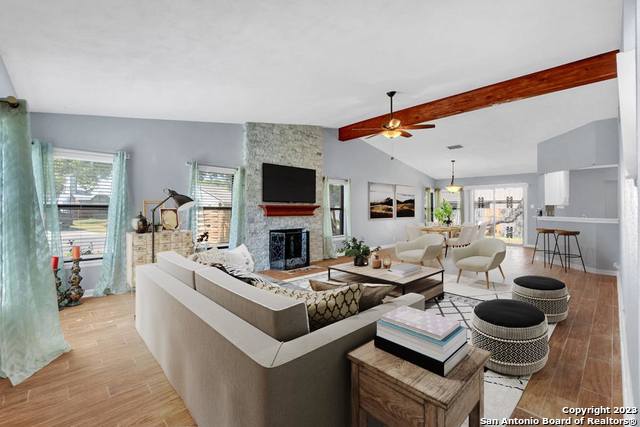 living room featuring light wood-type flooring, lofted ceiling with beams, a wealth of natural light, and a stone fireplace