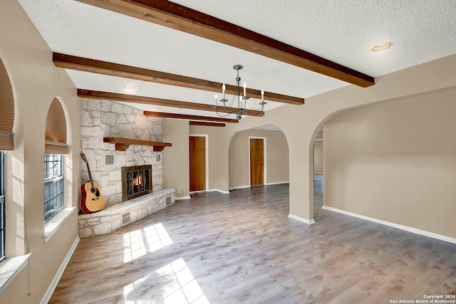 unfurnished living room featuring beamed ceiling, hardwood / wood-style flooring, a textured ceiling, and a stone fireplace