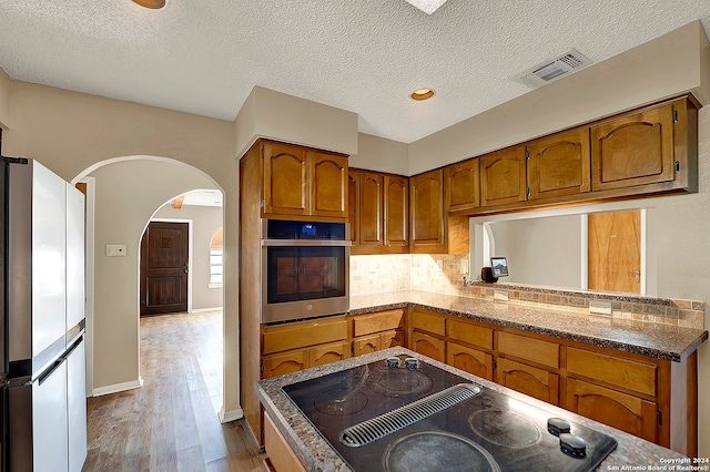 kitchen with a textured ceiling, oven, fridge, black electric cooktop, and light hardwood / wood-style floors