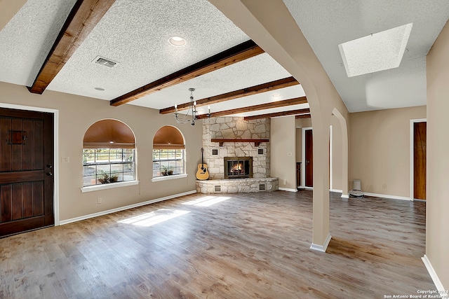 unfurnished living room with beamed ceiling, light hardwood / wood-style floors, and a textured ceiling