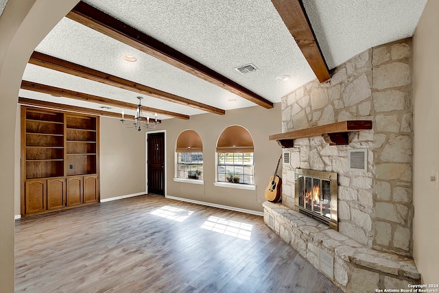 unfurnished living room featuring beamed ceiling, a stone fireplace, a chandelier, light hardwood / wood-style flooring, and a textured ceiling