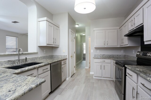 kitchen with light hardwood / wood-style floors, sink, light stone counters, stainless steel appliances, and white cabinetry