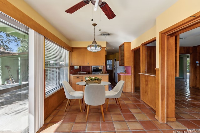 dining space featuring light tile patterned flooring, wood walls, and ceiling fan