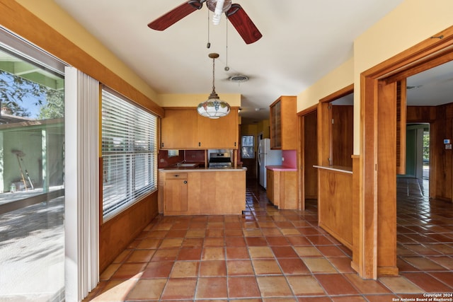 kitchen with ceiling fan, stainless steel refrigerator, kitchen peninsula, decorative light fixtures, and wood walls