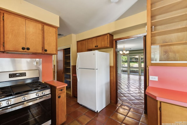 kitchen with white refrigerator, a notable chandelier, stainless steel gas stove, and dark tile patterned flooring