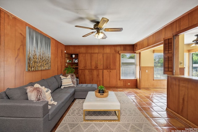 living room with ceiling fan, wood walls, and light tile patterned floors