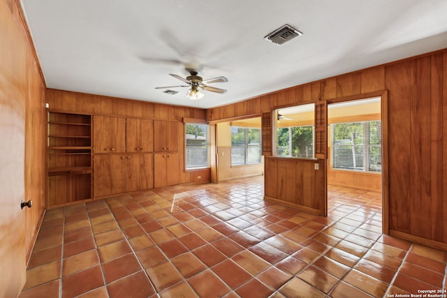 empty room featuring ceiling fan, wooden walls, built in shelves, and tile patterned floors