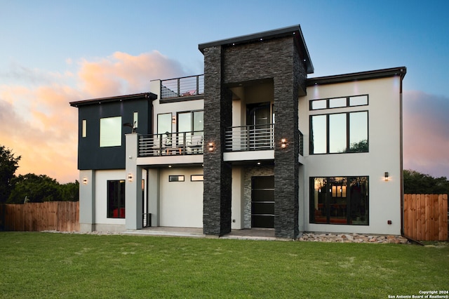 back house at dusk with a balcony and a yard