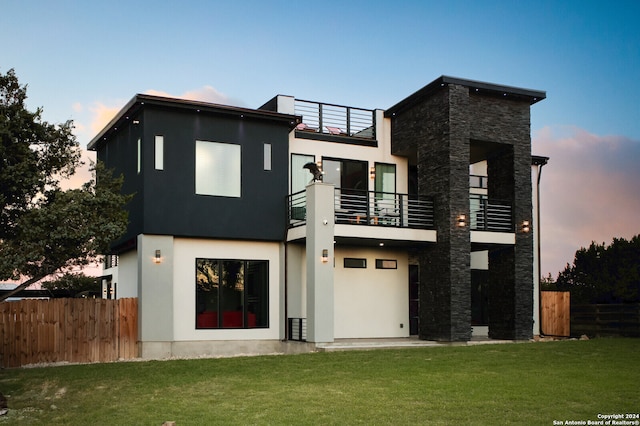 back house at dusk with a balcony and a yard