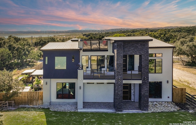 back house at dusk featuring a balcony and a lawn