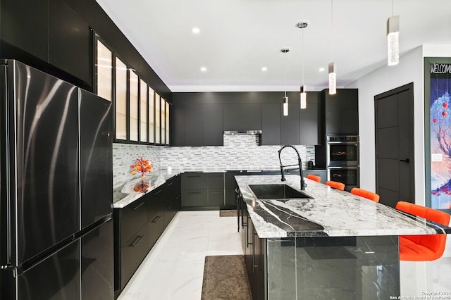 kitchen with decorative light fixtures, a center island with sink, backsplash, appliances with stainless steel finishes, and a breakfast bar