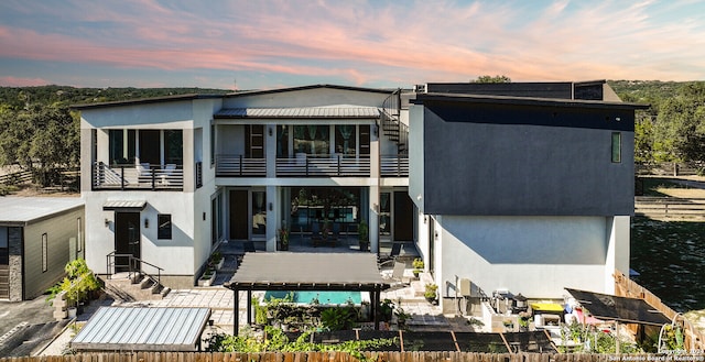 back house at dusk featuring a balcony and a patio