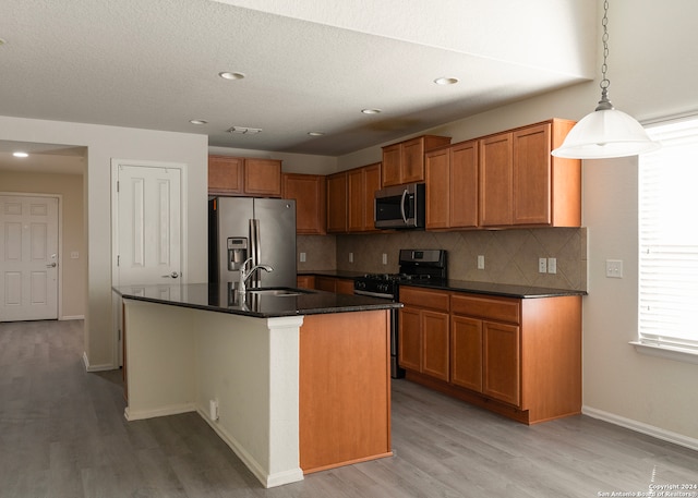 kitchen with a kitchen island with sink, light wood-type flooring, decorative light fixtures, sink, and stainless steel appliances