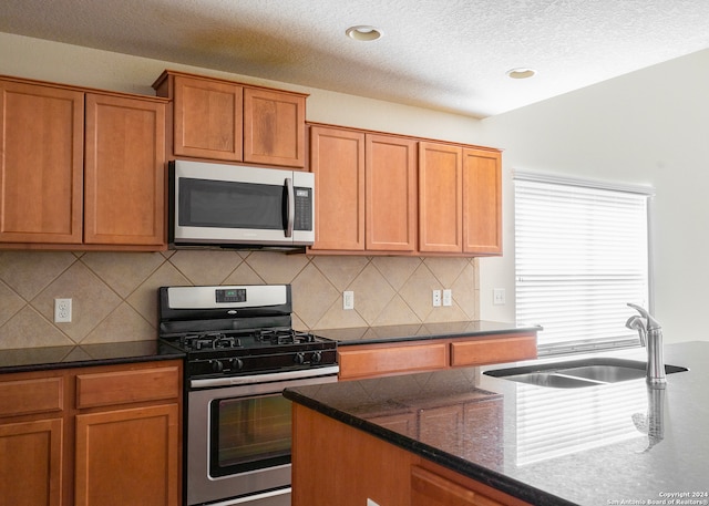 kitchen with appliances with stainless steel finishes, dark stone counters, decorative backsplash, and sink