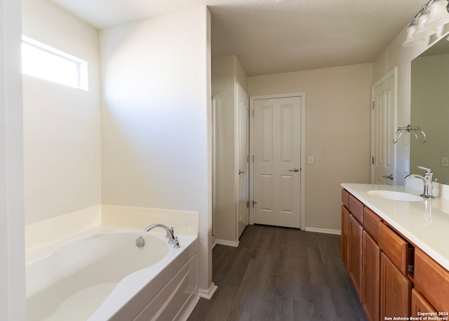 bathroom with wood-type flooring, a tub to relax in, vanity, and a textured ceiling