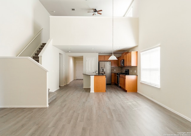 kitchen with a high ceiling, ceiling fan, pendant lighting, light hardwood / wood-style flooring, and stainless steel appliances