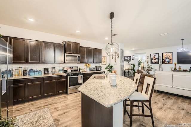 kitchen featuring light wood-type flooring, a kitchen breakfast bar, a center island with sink, decorative light fixtures, and appliances with stainless steel finishes