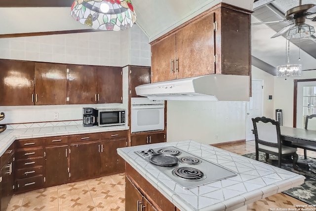 kitchen with lofted ceiling, white appliances, extractor fan, tile counters, and ceiling fan with notable chandelier