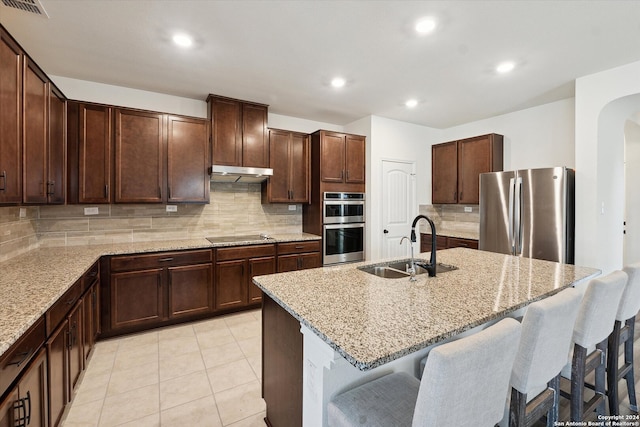 kitchen with stainless steel appliances, an island with sink, sink, and light stone counters