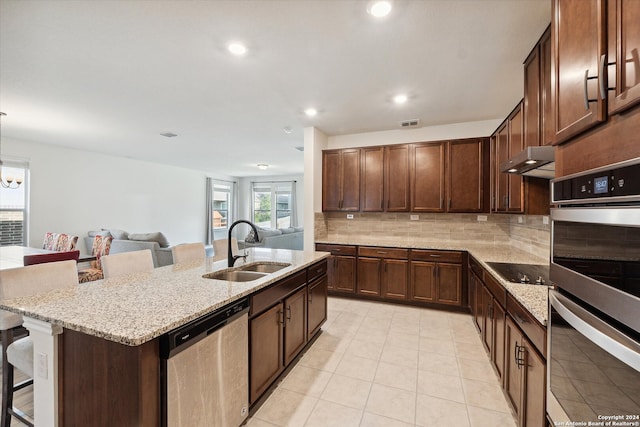 kitchen with an island with sink, stainless steel appliances, tasteful backsplash, sink, and a breakfast bar area