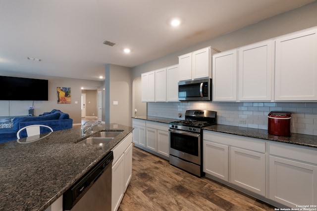 kitchen with appliances with stainless steel finishes, dark stone counters, dark wood-type flooring, and white cabinets