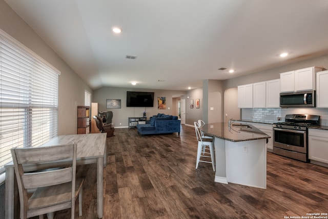 kitchen with appliances with stainless steel finishes, dark stone countertops, white cabinetry, and a center island with sink