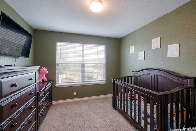 bedroom with a textured ceiling, a crib, and light colored carpet