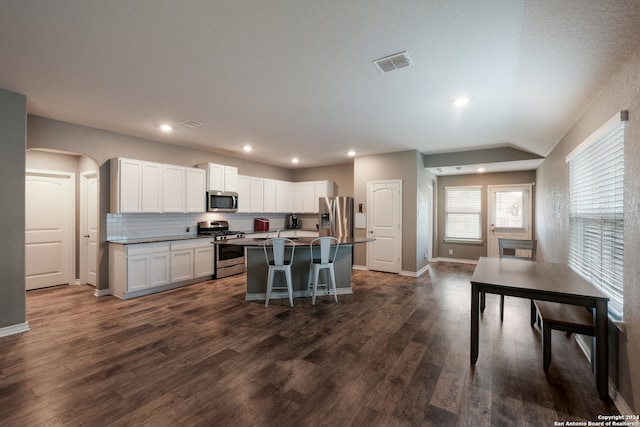 kitchen with white cabinets, an island with sink, dark wood-type flooring, appliances with stainless steel finishes, and a kitchen breakfast bar