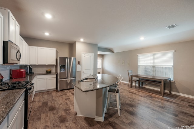 kitchen with dark wood-type flooring, white cabinets, appliances with stainless steel finishes, and a kitchen island with sink