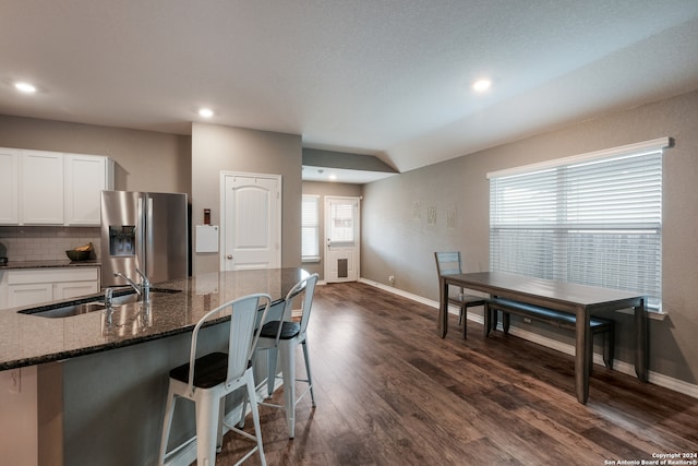 kitchen featuring a kitchen breakfast bar, dark stone countertops, dark hardwood / wood-style floors, white cabinets, and stainless steel fridge with ice dispenser