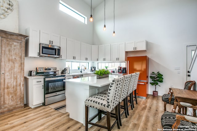 kitchen with a towering ceiling, a center island, hanging light fixtures, stainless steel appliances, and white cabinets