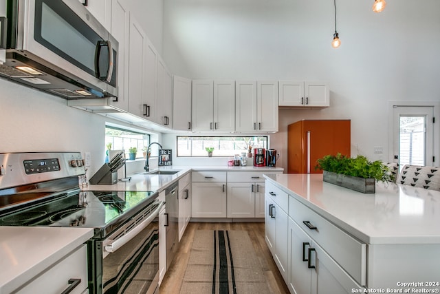 kitchen with sink, white cabinetry, light hardwood / wood-style floors, stainless steel appliances, and pendant lighting