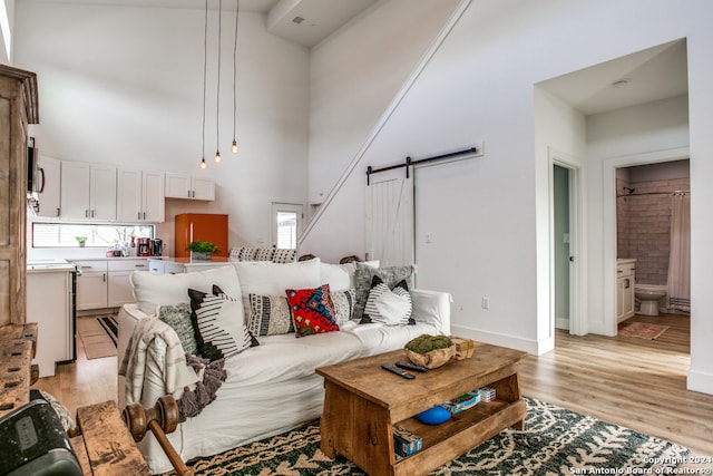 living room featuring a barn door, high vaulted ceiling, and light hardwood / wood-style floors