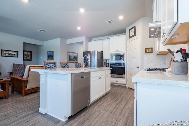 kitchen with light hardwood / wood-style flooring, a center island with sink, stainless steel appliances, backsplash, and white cabinets