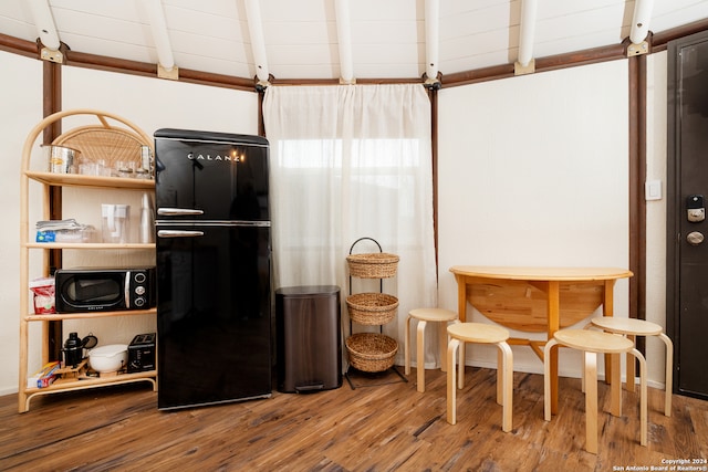 kitchen featuring beamed ceiling, hardwood / wood-style floors, and black refrigerator