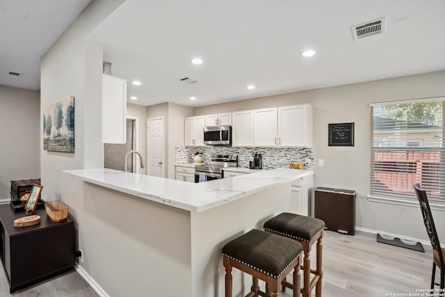 kitchen with appliances with stainless steel finishes, kitchen peninsula, white cabinets, and light hardwood / wood-style floors