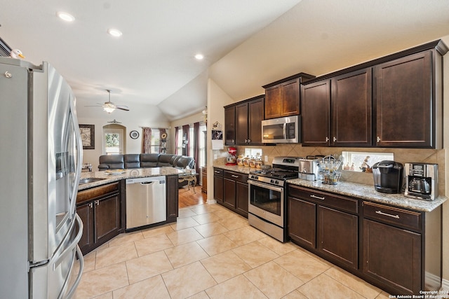 kitchen with ceiling fan, lofted ceiling, dark brown cabinets, appliances with stainless steel finishes, and light stone countertops