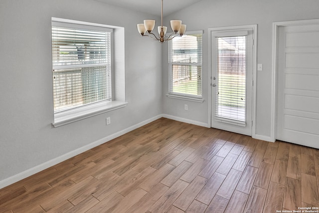 unfurnished dining area with vaulted ceiling, a chandelier, and light hardwood / wood-style floors