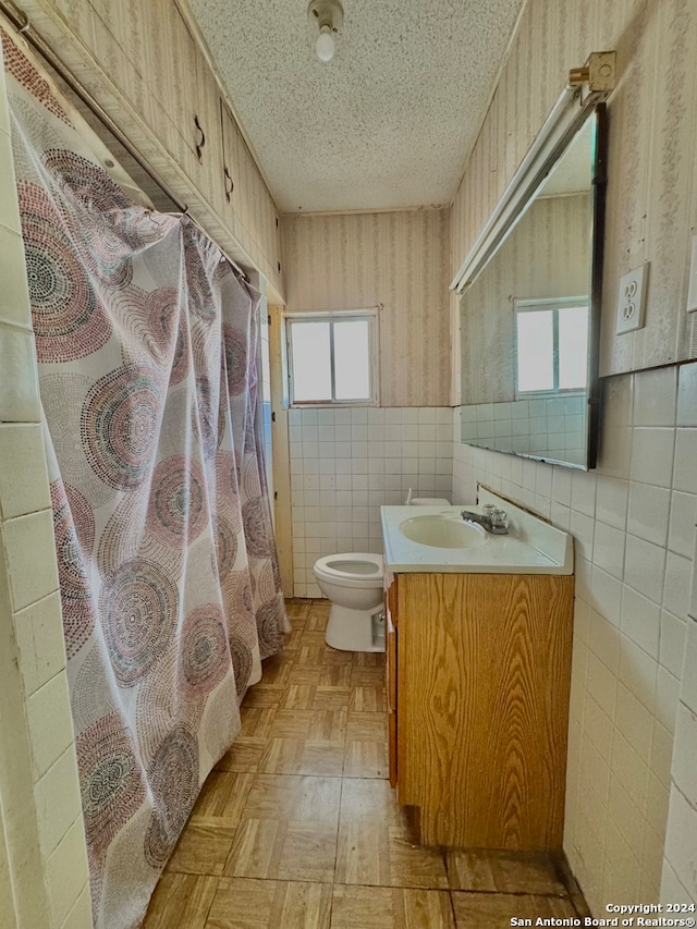 bathroom featuring a healthy amount of sunlight, toilet, tile walls, and vanity