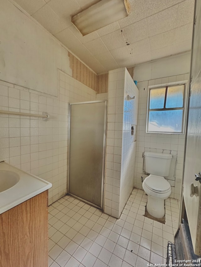 bathroom featuring tile patterned flooring, walk in shower, toilet, tile walls, and vanity