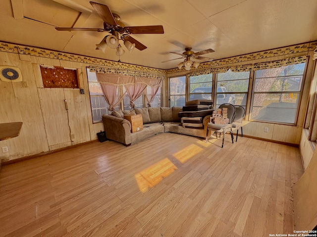 unfurnished living room featuring light wood-type flooring, a healthy amount of sunlight, ceiling fan, and wood walls