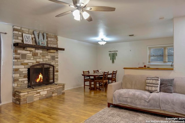 living room with ceiling fan, a stone fireplace, and wood-type flooring