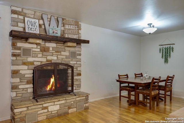 dining area featuring wood-type flooring and a stone fireplace