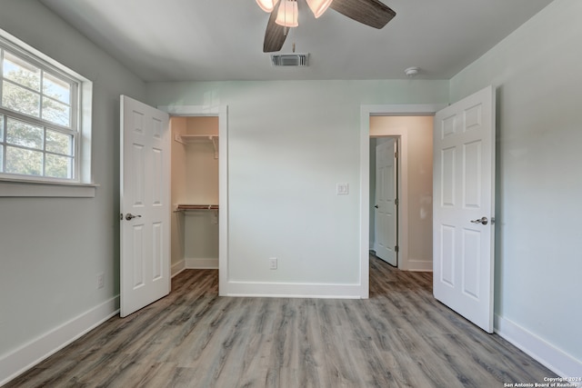 unfurnished bedroom featuring light wood-type flooring, a spacious closet, ceiling fan, and a closet